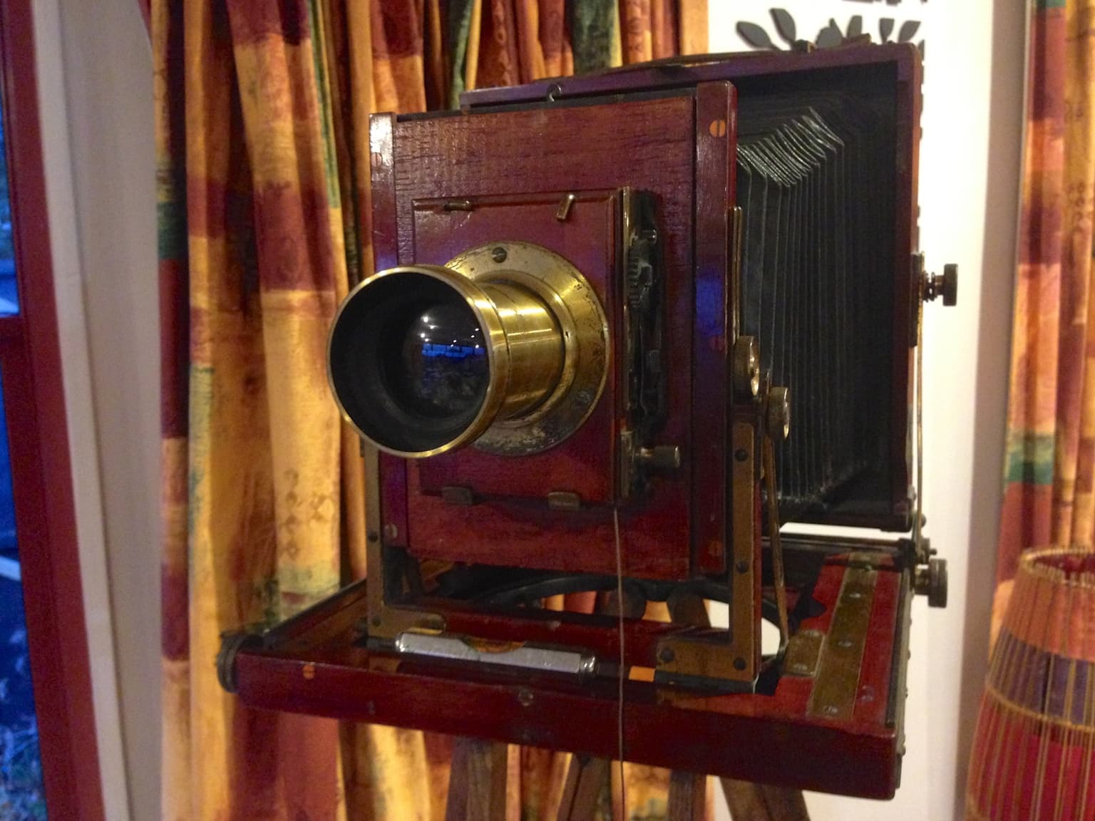 A mahogany and brass plate camera on a wooden tripod, bellows extended.